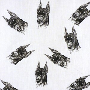May include: White fabric with a repeating pattern of black and gray Doberman Pinscher dog heads. The dog heads are drawn in a detailed, artistic style, with pointed ears and alert expressions. The design is evenly spaced across the fabric.
