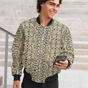 Puede incluir: Una chaqueta bomber beige con un patrón geométrico negro. La chaqueta tiene una cremallera y un cuello, puños y cintura de canalé.