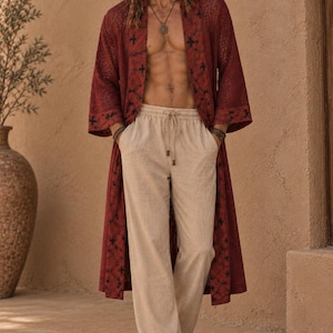 May include: A long-sleeved, open-front robe in a deep red hue featuring a dark, repeating cross-stitch pattern along the lapels and cuffs, paired with loose-fitting, beige drawstring trousers that have a simple, straight-leg design.