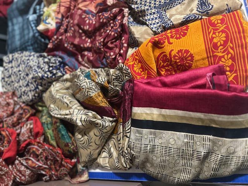 May include: A collection of colorful, patterned fabrics. The textiles display a variety of designs, including floral, geometric, and abstract patterns. Colors include red, yellow, blue, and cream. The fabrics appear to be silk or a similar lightweight material.