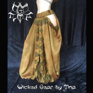 May include: A pair of flowing, patterned pants in shades of gold and olive green. The pants feature a unique design with cutouts and a central panel with intricate floral and paisley motifs. The text "Wicked Gear by Tina" is visible at the bottom.