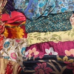 May include: A collection of colorful fabric pieces with floral and patterned designs. The fabrics include shades of red, blue, green, yellow, and pink. Some fabrics have intricate floral patterns, while others feature leaf and abstract designs.