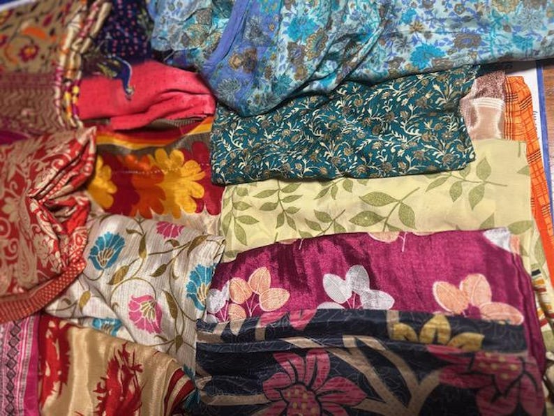May include: A collection of colorful fabric pieces with floral and patterned designs. The fabrics include shades of red, blue, green, yellow, and pink. Some fabrics have intricate floral patterns, while others feature leaf and abstract designs.
