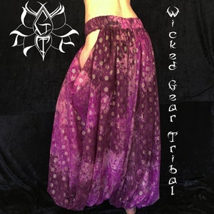 May include: Purple harem pants with a tie-dye effect and a floral pattern. The pants have a wide waistband and a loose, flowing fit. The text "Wicked Gear Tribal" is written vertically on the right side of the image.