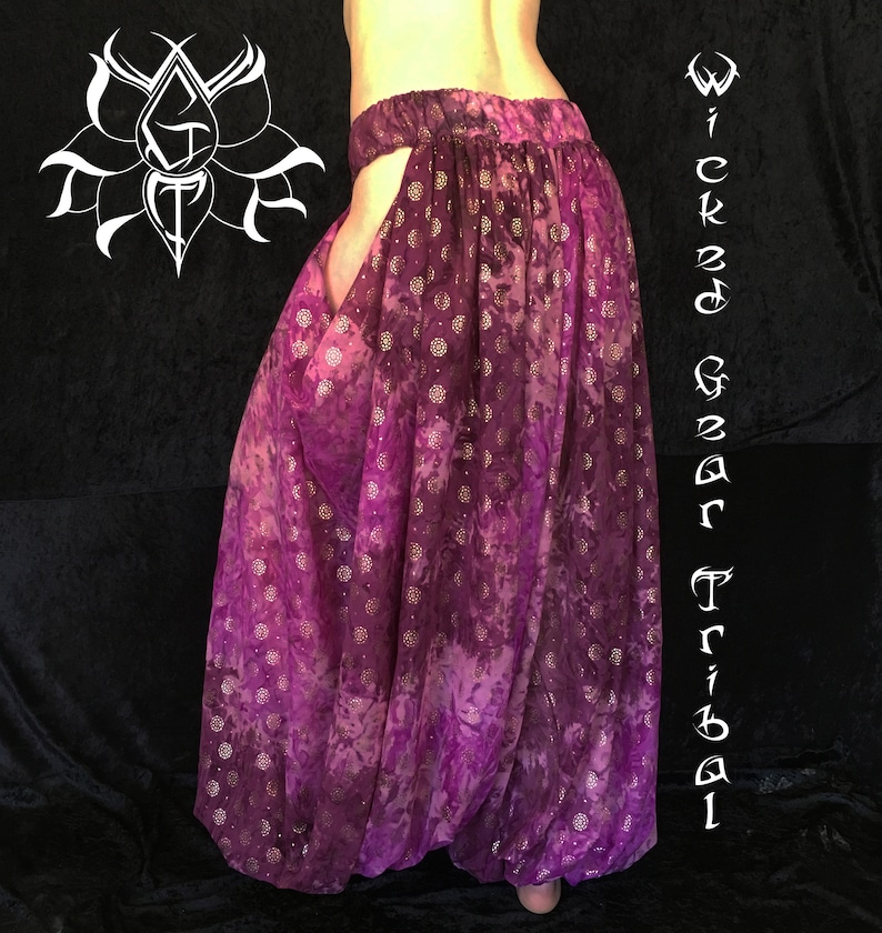 May include: Purple harem pants with a tie-dye effect and a floral pattern. The pants have a wide waistband and a loose, flowing fit. The text "Wicked Gear Tribal" is written vertically on the right side of the image.