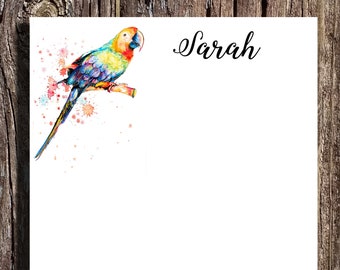 May include: A colourful watercolour painting of a parrot perched on a branch with a white background and the name "Sarah" written in black cursive.