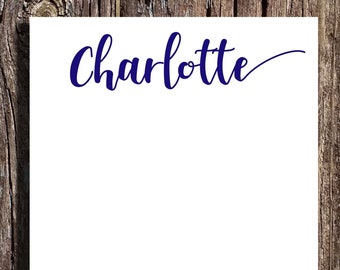 May include: A white notepad with the name "Charlotte" written in blue cursive script on the top.