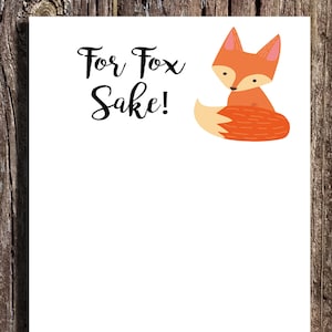 May include: A white card with the text "For Fox Sake!" in black cursive font. A cartoon fox with orange fur and a white belly is sitting on its haunches with its tail curled around its body.
