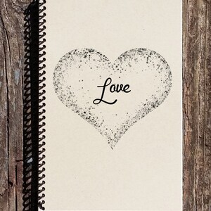 May include: A spiral bound notebook with a cream colored cover. The cover features a black and white heart shape with the word "Love" written inside.