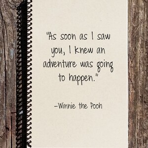 May include: A white notebook with a black spiral binding. The notebook has a quote from Winnie the Pooh written on it: "As soon as I saw you, I knew an adventure was going to happen."