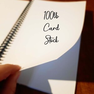 May include: A close-up of a white spiral bound notebook with the text "100lb Card Stock" written on the cover.