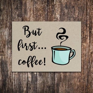 May include: A brown card with the text "But first... coffee!" in black cursive font. A cartoon illustration of a blue coffee mug with steam rising from it is to the right of the text.