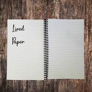 May include: An open spiral bound notebook with lined paper. The front cover has the words "Lined Paper" written in black ink.