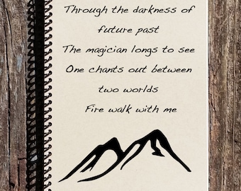 May include: A notebook with a black spiral binding and a handwritten poem about a magician and fire. The poem reads: "Through the darkness of future past The magician longs to see One chants out between two worlds Fire walk with me". The notebook has a black ink drawing of two mountains at the bottom.