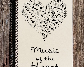 May include: A cream-coloured spiral bound notebook with a black heart shape made of musical notes. The text "Music of the Heart" is printed below the heart.
