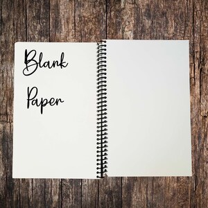 Puede incluir: Un cuaderno abierto de espiral con papel blanco en blanco. Las palabras "Blank Paper" est&aacute;n escritas en la p&aacute;gina izquierda.