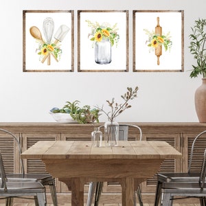 May include: Three framed watercolor prints with a kitchen theme. The prints feature a mason jar with sunflowers, a rolling pin with sunflowers, and a whisk, spatula, and wooden spoon with sunflowers.
