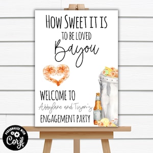 May include: A white sign with black text that reads "How sweet it is to be loved Bayou".  The sign also has a heart made of two prawns, a bucket of crawfish, and a bottle of beer.  The text "Welcome to Abbylane and Tigon's Engagement Party" is at the bottom of the sign.