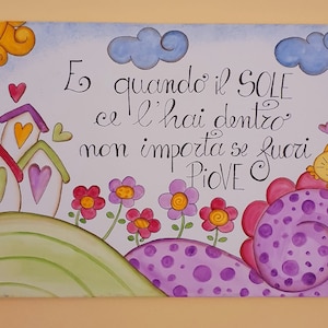 Peut inclure: Une peinture colorée avec une citation en italien qui dit "E quando il SOLE ce l'hai dentro non importa se fuori PIOVE". La peinture représente un soleil, des nuages, des maisons, des fleurs et un chat.