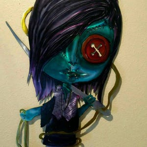 May include: A metal wall art piece depicting a stylized doll with teal skin, black hair with purple highlights, and a large red button eye. The doll holds scissors and string, wearing a vest and a stitched mouth.