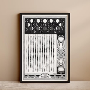 Op de afbeelding: Zwart-wit ingelijste kunstprint met een gedetailleerde illustratie van de maanfasen voor het jaar 2026. Het ontwerp bevat de tekst "THE MOON" en een decoratieve rand. De print wordt gepresenteerd in een zwarte lijst.
