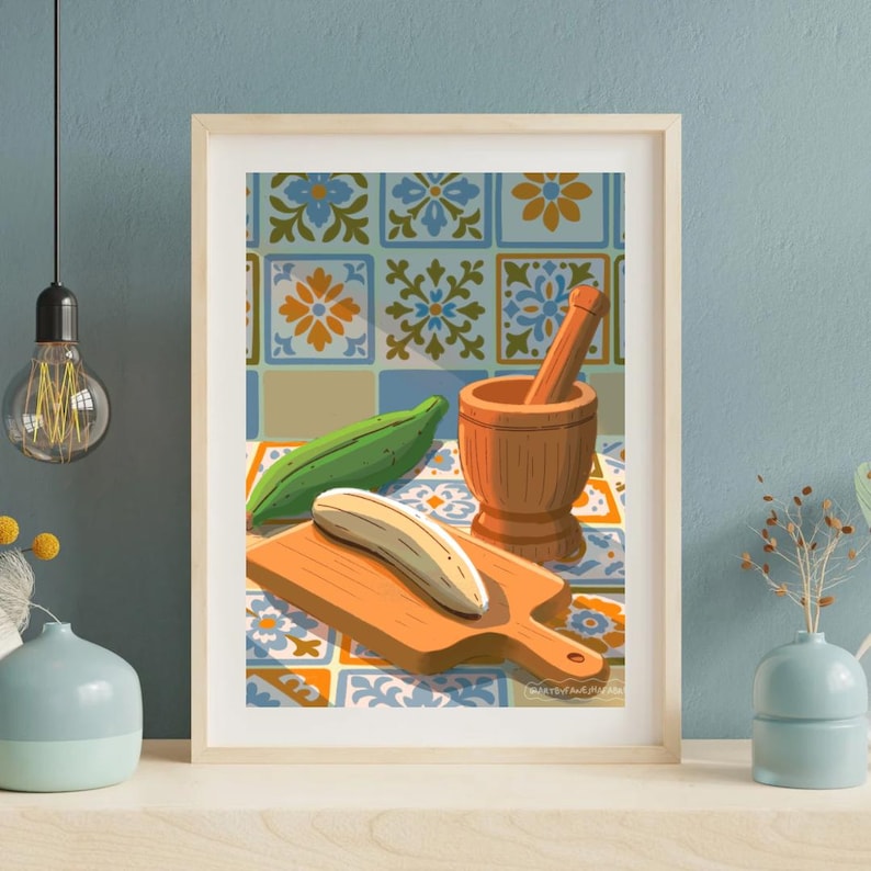 Op de afbeelding: Een ingelijste kunstdruk met een stilleven van keukenartikelen. Een houten vijzel en stamper, een groene groente en een banaan liggen op een houten snijplank. De achtergrond heeft een tegelontwerp.