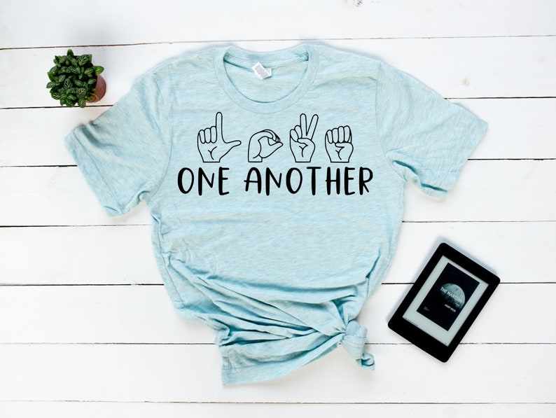 May include: Light blue t-shirt with the word "LOVE" spelled out in American Sign Language and the words "ONE ANOTHER" printed below.