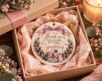 May include: A round white ceramic ornament featuring a dusty pink bow at the top and a wreath of greenery and pink berries. The center text reads Thank you FOR KEEPING MY HOME Sparkling, with illustrations of a cleaning bucket, spray bottle, and cloth.