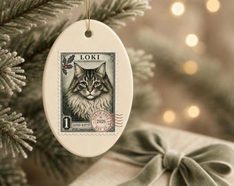 May include: An oval-shaped white ceramic ornament featuring a postage stamp graphic of a long-haired tabby cat. The stamp includes the text LOKI, 1, GOOD KITTY, and a North Pole 2026 postmark with holly leaves in the corner.