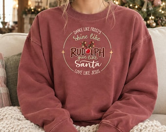 May include: A brick red crewneck sweatshirt featuring a circular graphic with the text: Dance like Frosty, Shine like Rudolph, Give like Santa, Love like Jesus. The design includes a red nose and brown reindeer antlers above the text.