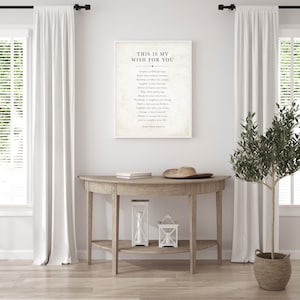 May include: A white framed print with a black and white inspirational quote that reads "This is my wish for you." The quote is by Ralph Waldo Emerson. The print is hanging on a white wall above a wooden console table with two white lanterns.