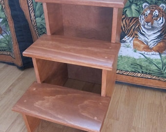 May include: A three-step wooden stool with a natural wood finish. The stool has three steps and a small shelf on the top step.