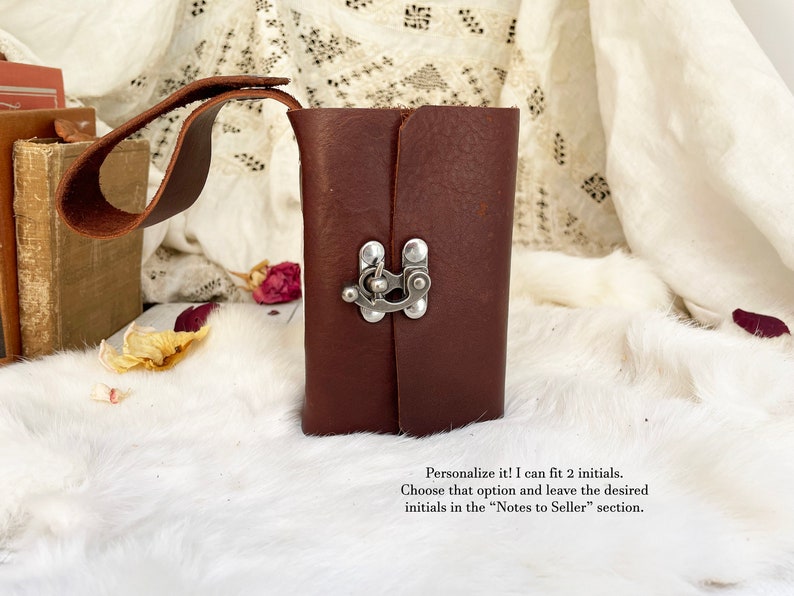 May include: A dark brown leather journal with a silver clasp closure and a matching leather handle. The journal is rectangular and appears to be handmade. The text on the image says, "Personalize it! I can fit 2 initials."