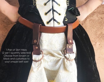 May include: A brown leather belt with skirt hikes attached. The skirt hikes are made of brown leather and copper-colored metal rings. The text on the image reads: "1 Pair of Skirt Hikes (2 per 1 quantity selected) Choose from brown or black and customize to your unique belt size!"