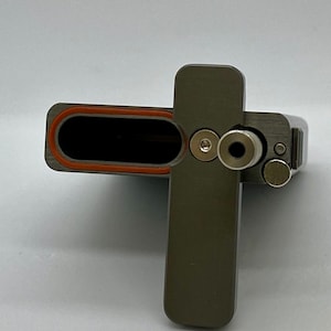 May include: A gray metal box with a hinged lid and a small, round hole on the side. The box has a red rubber seal around the opening.