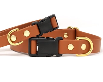 Peut inclure: Deux colliers pour chiens de couleur marron clair, avec des boucles en plastique noir et des accessoires métalliques dorés. Les colliers sont fabriqués dans un matériau lisse semblable au cuir. Un collier est à plat, l'autre est partiellement bouclé.