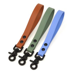 May include: Three wrist straps in shades of brown, green, and blue. Each strap has a black metal clasp and two black rivets. The straps are made of a smooth, flexible material.