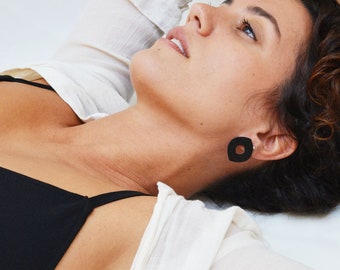 May include: A woman with curly brown hair wearing a black bra and a white shirt with a black square earring.