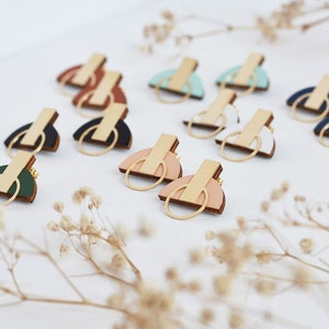 May include: A set of geometric wooden earrings with gold accents. The earrings are in various colours, including green, blue, white, and pink.