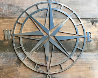 Op de afbeelding: Een zilveren metalen kompas met een stervormig ontwerp en de letters N, S, E en W. Het kompas bevindt zich op een houten achtergrond.