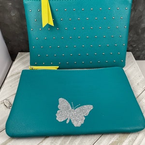 May include: Two teal cosmetic bags. The top bag has silver studs and a yellow zipper pull. The bottom bag has a silver glitter butterfly design. Both bags have yellow zippers.