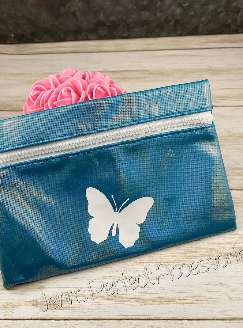 May include: Teal-colored zippered pouch with a white butterfly design. The pouch has a white zipper and is made of a shiny material. The words "Jenns Perfect Accessories" are printed on the bottom right.