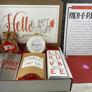 May include: A gift box with various items, including a flask with "MENOPAUSE...don't judge" text, a burlap bag with "XOXO", and a card that says "MEN-O-PAUSE". Other items include a fan, shower melts, and a box of chocolates.
