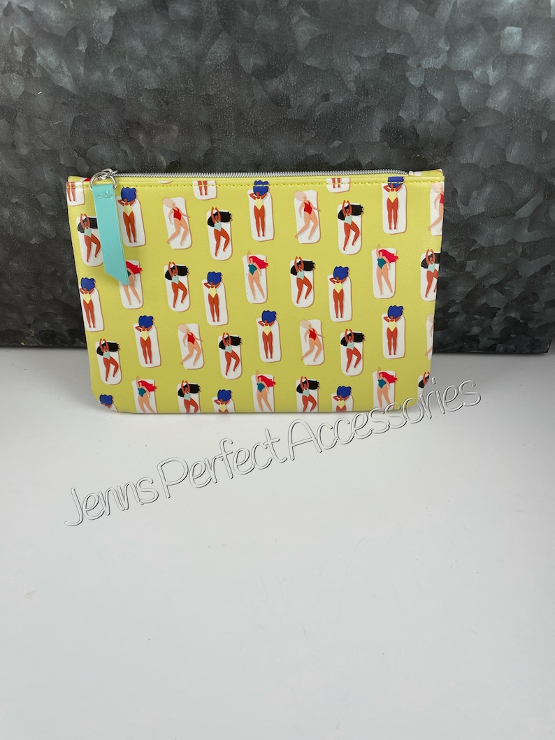 May include: A yellow cosmetic bag with a repeating pattern of women in swimsuits sunbathing on beach towels. The bag has a teal zipper pull and the text "Jenns Perfect Accessories".