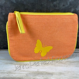 May include: Orange canvas zippered pouch with a yellow butterfly applique. The pouch has a yellow zipper and trim, and a yellow tassel on the zipper pull. The text "Jenns Perfect Accessories" is printed on the bottom.