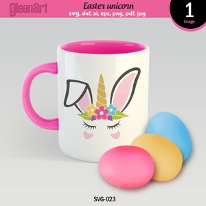 May include: A white ceramic mug with a pink rim and handle, featuring a cartoon bunny unicorn with a gold horn and a flower crown. The mug is sitting on a white surface next to three pastel-colored Easter eggs.