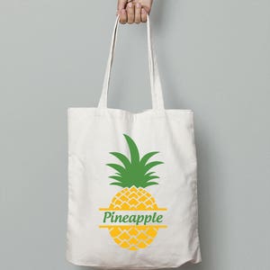 Puede incluir: Una bolsa de tela blanca con un gráfico de piña amarilla y la palabra "Pineapple" escrita en una pancarta verde en el medio de la piña.