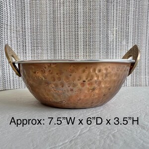 May include: A hammered copper bowl with two decorative brass handles and a silver-toned rim. The bowl features a rounded base and a wide opening. Text printed on the image indicates dimensions of approximately 7.5 inches wide, 6 inches deep, and 3.5 inches high.