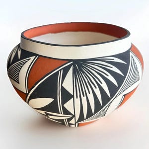 May include: A hand-painted ceramic bowl with a wide, rounded shape. The bowl features a white interior and rim, with a terracotta-colored band around the top. The exterior is decorated with black and white geometric patterns and shapes. A unique piece of pottery.