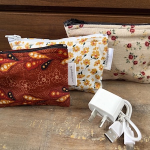 Può includere: Tre pochette in tessuto con cerniera di varie dimensioni con stampe floreali e motivi nei colori arancione ruggine, giallo e crema. Ogni pochette ha un'etichetta laterale bianca con la scritta LisaDesignsHQ e una chiusura a cerniera.